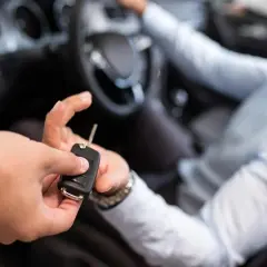 En person lämnar över bilnycklar till en leende man i förarsätet, redo för en ny resa eller kanske en avskrivning bil.