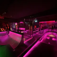En neonupplyst minigolfbana i Göteborg med rosa och grönt ljus. En person står vid en bana.