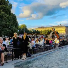 Folk njuter av en sommarkväll med mat och dryck vid fontänen, kanske efter en gratis konsert i Stockholm.