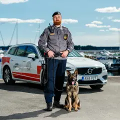 En skyddsvakt med hund står vid en bil i en hamn. Deras arbete kräver noggrann skyddsvakt utbildning.
