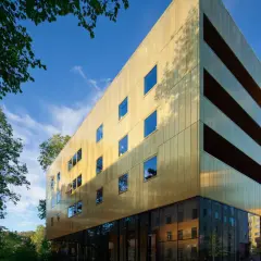 Sven-Harrys konstmuseum glänser i guld under en klarblå himmel. Gröna träd ramar in den moderna byggnaden.