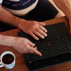 Två personer vid ett träbord planerar sin Swedbank budget. En kopp kaffe och ett glas juice står bredvid en öppen laptop.