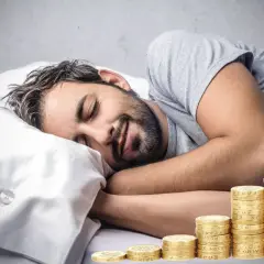 Man sover lugnt bredvid en växande stapel mynt, en dröm om passiva inkomster som blir verklighet.