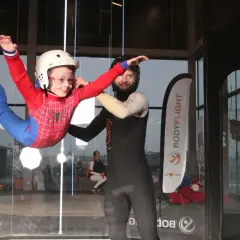 Barn i Spindelmannen-dräkt flyger i vindtunnel, en av många roliga aktiviteter i Stockholm. En instruktör hjälper till.