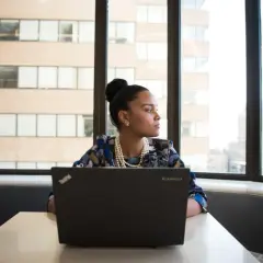 Kvinna med laptop vid fönstret, redo att plugga upp betyg distans.