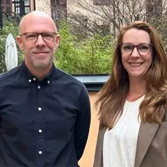 Två leende personer, en man och en kvinna, står utomhus. Kanske är de kollegor som diskuterar vinnova lediga jobb.