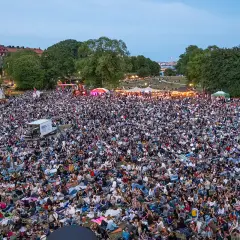 Stor publik samlad för utomhusbio i Stockholm. Tusentals människor sitter på filtar i en park och tittar mot en scen.