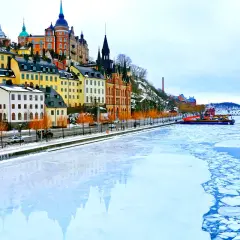 Färgstarka hus längs vattnet i Stockholm på vintern, med isflak som driver i vattnet.