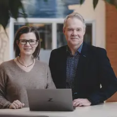 Två kollegor ler vid en laptop. De är på ett kontor i Stockholm, kanske för en praktik.