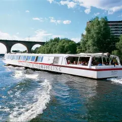 Sightseeingbåt passerar under en gammal tegelbro i Stockholm. Vattnet skummar bakom båten.