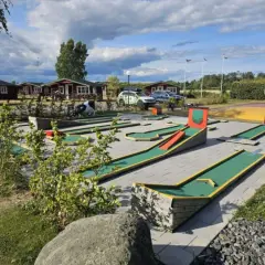 En minigolfbana vid Slottsskogen med röda stugor i bakgrunden. En ko-staty står vid en bana.