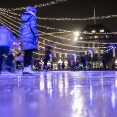 Människor njuter av kungsträdgården ice skating under gnistrande ljus. Isen reflekterar den magiska stämningen.
