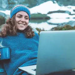 Kvinna med mugg och laptop i fjällen, studerar konstvetenskap distans.