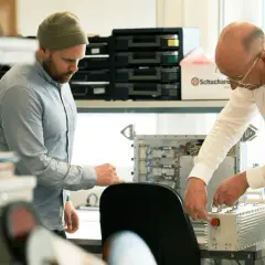Två män arbetar med elektronik. En creative director ser på när en kollega kopplar ihop komponenter.