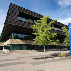 Modern byggnad med stenfasad och mörka träpaneler. En blå skylt med "Stockholms universitet" står bredvid. En del av universitet i Stockholm lista.
