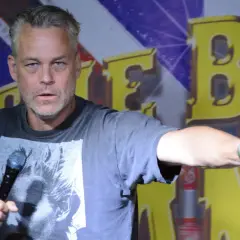 En stand up komiker i Sverige pekar med ena handen och håller en mikrofon i den andra.