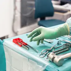 Steriltekniker utbildning: En hand i grön handske plockar bland sterila kirurgiska instrument på ett operationsbord.