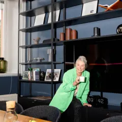En glad hr specialist med en grön kavaj dricker kaffe framför en bokhylla.