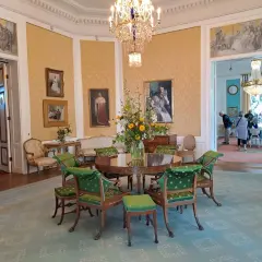 Elegant room with a round table, green chairs, floral arrangement, and paintings on yellow walls.