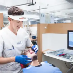 En tandhygienist i skyddsutrustning utför en undersökning på en patient. Detta är en del av en tandhygienist utbildning.
