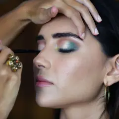 En makeupartist utför en professionell utbildning. En kvinna får en grön och silverfärgad ögonsminkning.