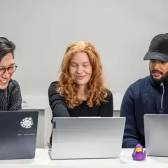 Tre personer arbetar vid sina laptops. En data scientist med rött hår ler.