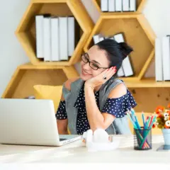 Kvinna ler vid sin laptop, omgiven av böcker och blommor. Hon verkar njuta av sin tid med **academy online**.