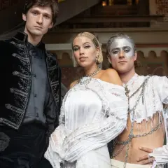 Tre personer i fantasifulla kläder. En man i svart sammetsjacka, en kvinna i en vit klänning som en **vita duken**, och en man med silvermålat ansikte i en trasig vit skjorta med kedjor.
