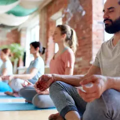 Människor med slutna ögon sitter i lotusställning på yogamattor. En grupp som deltar i en yoga utbildning distans.