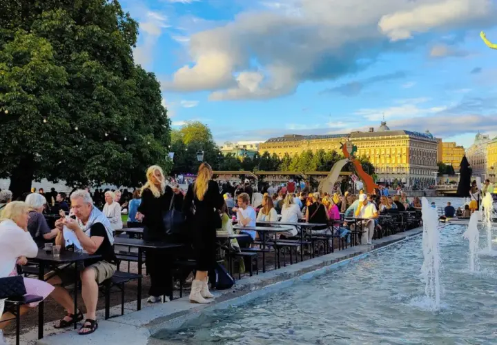 Folk njuter av en sommarkväll med mat och dryck vid fontänen, kanske efter en gratis konsert i Stockholm.