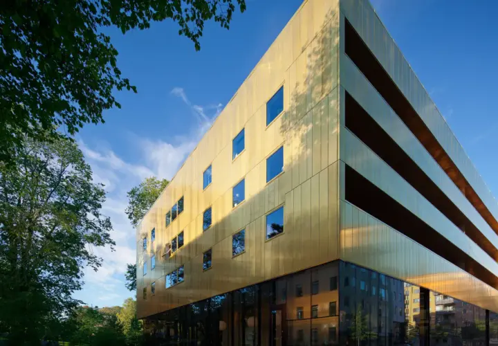 Sven-Harrys konstmuseum glänser i guld under en klarblå himmel. Gröna träd ramar in den moderna byggnaden.