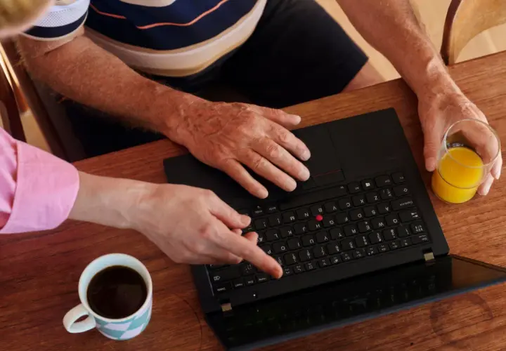 Två personer vid ett träbord planerar sin Swedbank budget. En kopp kaffe och ett glas juice står bredvid en öppen laptop.