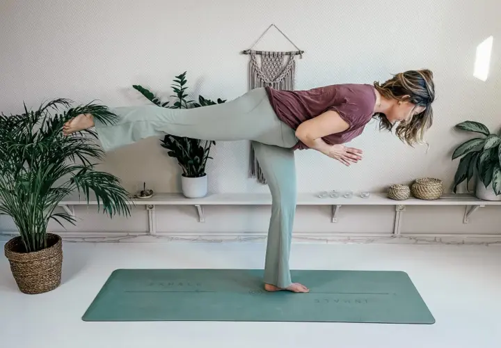 Kvinna utför yogapositionen Krigare III på en grön matta i Haninge. Hennes kropp är parallell med golvet, med ena benet utsträckt bakåt.