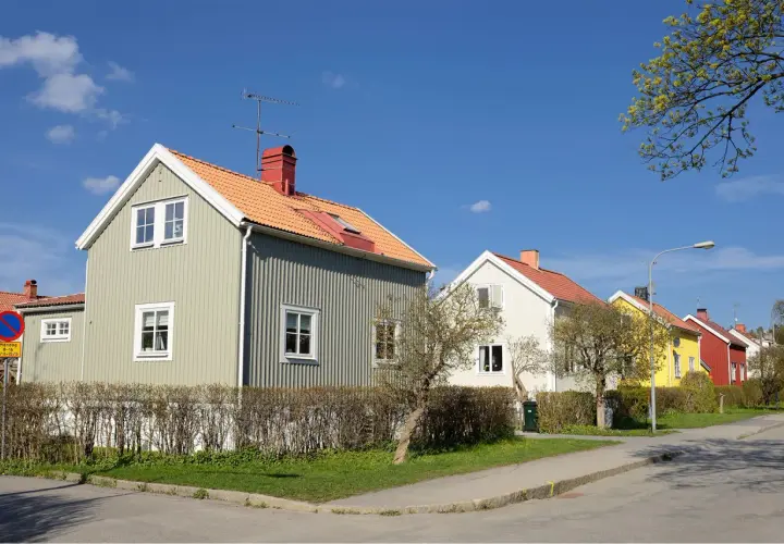 Rad av charmiga trähus i olika färger, med orange tak och gröna fasader. En dröm om ett hem med rimlig belåningsgrad.