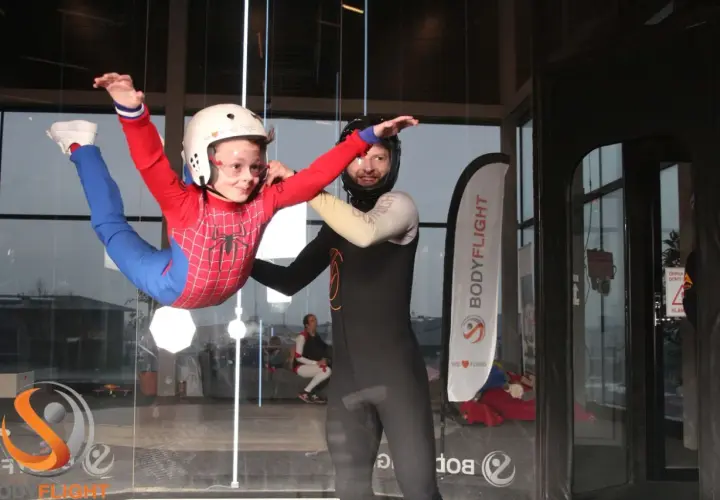 Barn i Spindelmannen-dräkt flyger i vindtunnel, en av många roliga aktiviteter i Stockholm. En instruktör hjälper till.