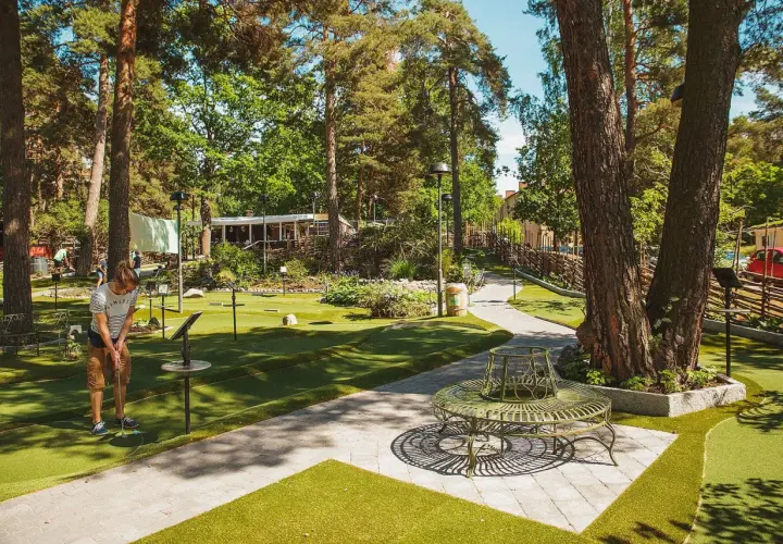 En person spelar minigolf i Aspudden, omgiven av grönska och träd. En vacker sommardag för en runda minigolf.