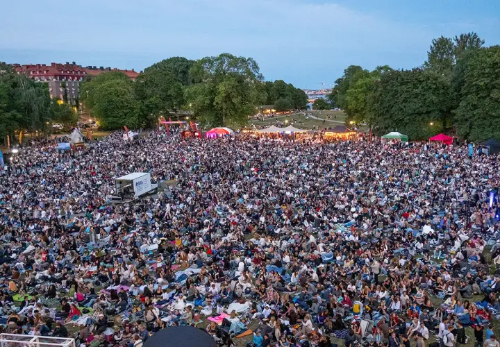 Stor publik samlad för utomhusbio i Stockholm. Tusentals människor sitter på filtar i en park och tittar mot en scen.
