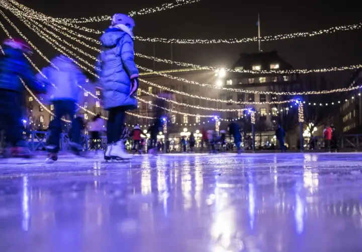 Människor njuter av kungsträdgården ice skating under gnistrande ljus. Isen reflekterar den magiska stämningen.