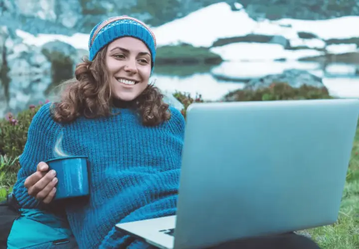Kvinna med mugg och laptop i fjällen, studerar konstvetenskap distans.