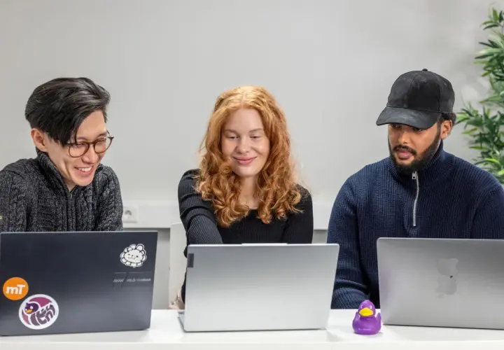 Tre personer arbetar vid sina laptops. En data scientist med rött hår ler.