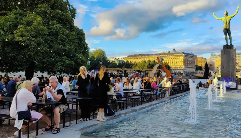 Folk njuter av en sommarkväll med mat och dryck vid fontänen, kanske efter en gratis konsert i Stockholm.
