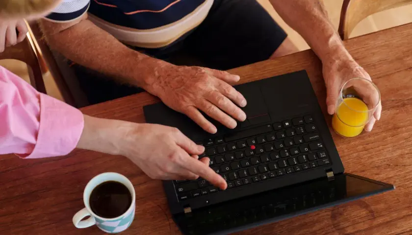 Två personer vid ett träbord planerar sin Swedbank budget. En kopp kaffe och ett glas juice står bredvid en öppen laptop.