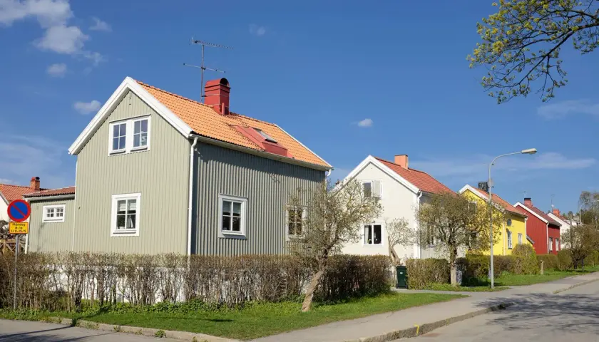 Rad av charmiga trähus i olika färger, med orange tak och gröna fasader. En dröm om ett hem med rimlig belåningsgrad.