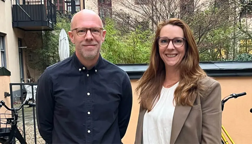Två leende personer, en man och en kvinna, står utomhus. Kanske är de kollegor som diskuterar vinnova lediga jobb.
