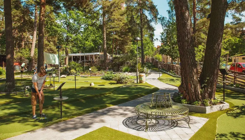 En person spelar minigolf i Aspudden, omgiven av grönska och träd. En vacker sommardag för en runda minigolf.