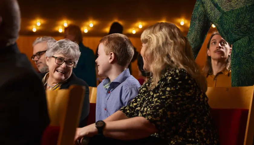 En familj njuter av en klassisk konsert. En mormor ler, ett barn tittar nyfiket framåt och en ung man i bakgrunden lyssnar uppmärksamt.