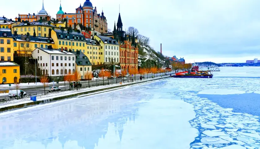 Färgstarka hus längs vattnet i Stockholm på vintern, med isflak som driver i vattnet.