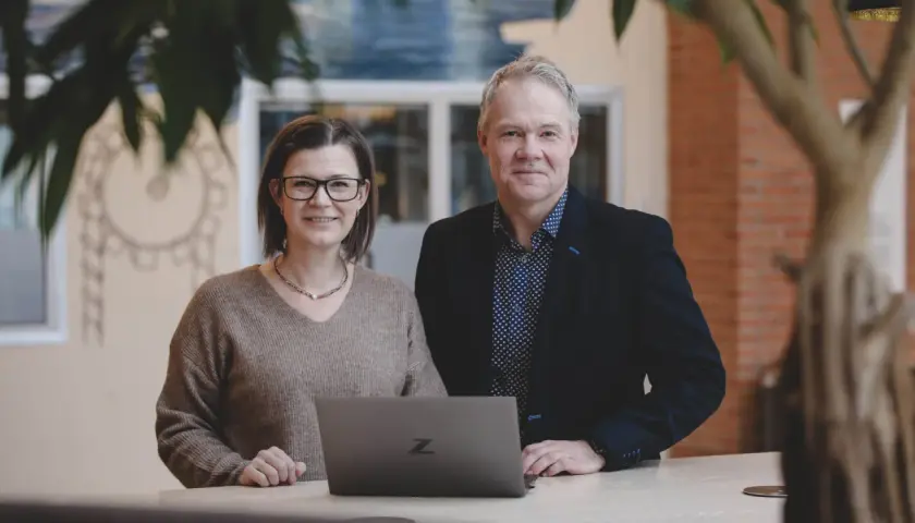Två kollegor ler vid en laptop. De är på ett kontor i Stockholm, kanske för en praktik.