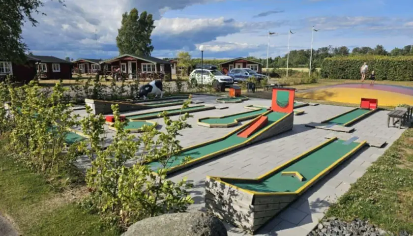 En minigolfbana vid Slottsskogen med röda stugor i bakgrunden. En ko-staty står vid en bana.