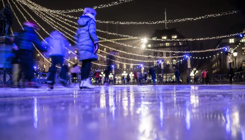 Människor njuter av kungsträdgården ice skating under gnistrande ljus. Isen reflekterar den magiska stämningen.